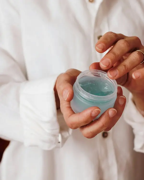 Mãos abrindo um pote de gel hidratante azul-claro
