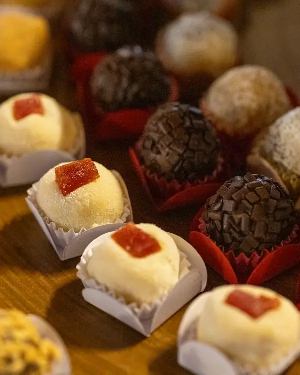 Brigadeiros e beijinhos em forminhas sobre mesa de madeira