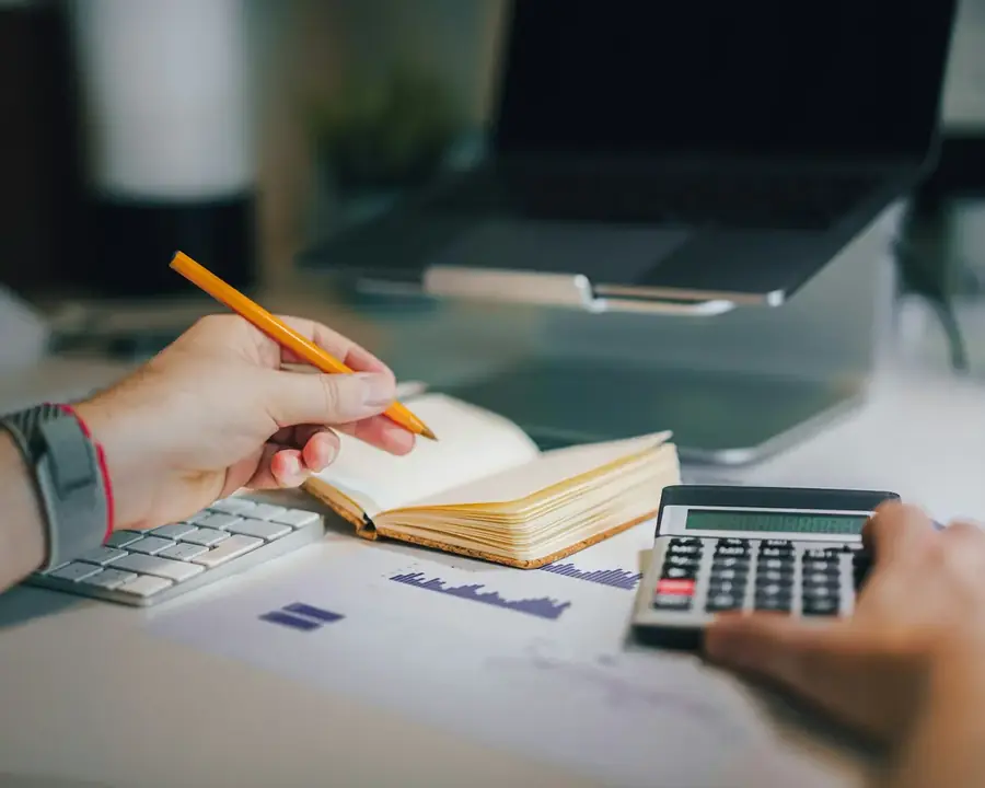 Mãos fazem contas na calculadora ao lado de um caderno e de relatórios