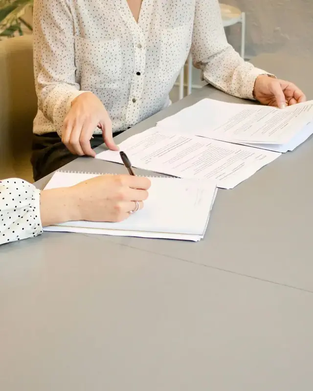 Duas pessoas revisam e assinam documentos sobre a mesa
