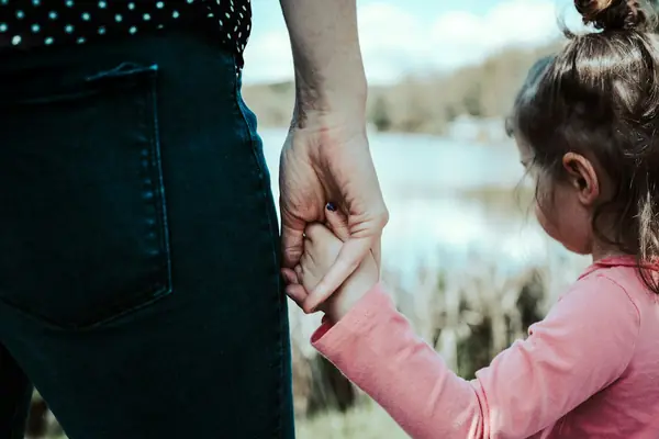 Mãe e filha de mãos dadas à beira de um lago