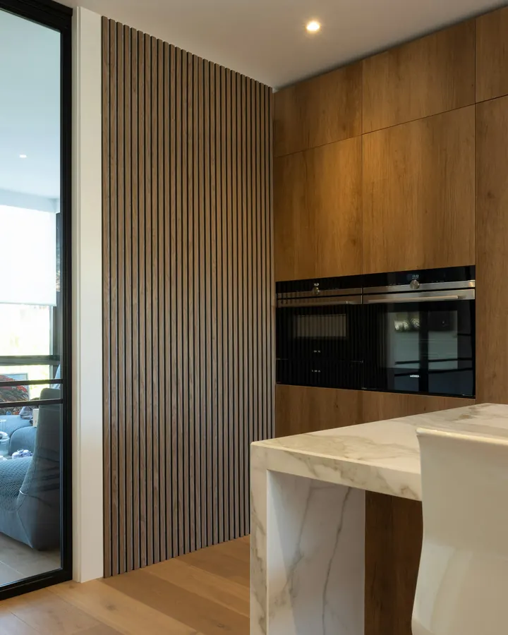 Cozinha com painel ripado, marcenaria de madeira e ilha de mármore